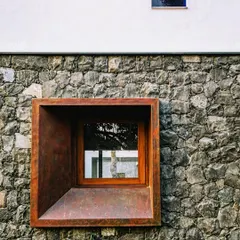 A deeply recessed window in a stone wall creates a beautifully framed view. The rusted steel box provides shade and adds a layer of texture and color, transforming a simple opening into a significant architectural feature.