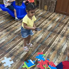 A toddler works on a large floor puzzle of Clifford. Puzzles are excellent for developing problem-solving skills and spatial awareness.
