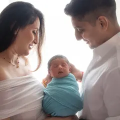 Welcoming their newborn with so much love. The parents' adoring smiles and the baby peacefully wrapped in blue create a perfect first family photo.
