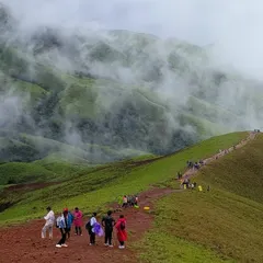A group of trekkers makes their way along the winding path of Netravathi peak. This image shows the scale of the landscape and the shared experience of the journey.