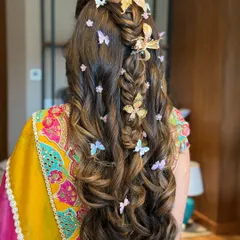 For a playful and whimsical Mehandi look, I created this half-up, half-down style featuring a fishtail braid and voluminous curls. The look is brought to life with an array of delicate butterfly clips in gold and pastel shades, adding a touch of magic.