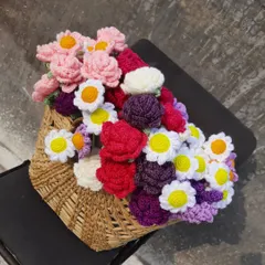 A traditional wicker basket filled with a colorful assortment of handmade crochet flowers. This shows how they can be displayed in a shop or used as a beautiful, permanent floral arrangement.