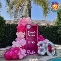 A Barbie theme is perfect for a glamorous celebration. This setup for a 30th birthday featured a life-sized Barbie box for photos, framed by a cascade of pink balloons and large silver foil numbers.