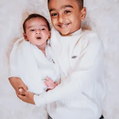 A sweet and funny interaction between brothers. The newborn's surprised expression and the big brother's happy grin make for a perfect candid sibling portrait.