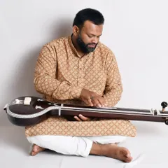 Demonstrating the playing position for the flat wooden tanpuri. Its smaller, flatter body makes it easier to handle and travel with compared to a traditional gourd tanpura.