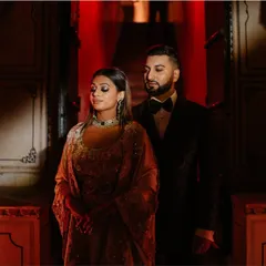 A stylish couple portrait from a sangeet and reception event at Mundota Palace. The dramatic red lighting and their elegant attire create a feeling of glamour and romance.