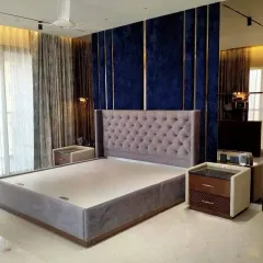 A fully upholstered bed with a deep-buttoned, winged headboard. This piece was created for a client who wanted a luxurious, hotel-like feel for their bedroom. The royal blue velvet wall paneling with metal inlays adds to the drama.