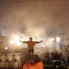 A powerful silhouette shot of me on stage, arms outstretched in front of a massive crowd, with smoke and bright lights creating a dramatic effect.