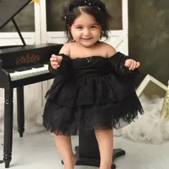 A sweet smile from a little musician. This baby girl's happiness is contagious as she stands by her miniature black piano in this elegant studio setup.