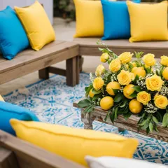 A casual and chic seating arrangement with wooden benches, bright yellow and blue cushions, and a centerpiece of lemons and roses. The patterned rug adds another layer of Mediterranean-inspired design.