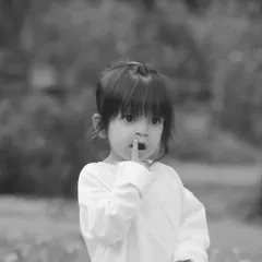 "Shhh." A little girl puts her finger to her lips in this classic black and white outdoor portrait. This style creates a timeless, storytelling feel.