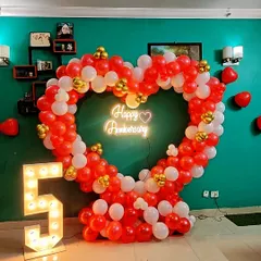 This vibrant heart-shaped balloon arch in red and white makes a bold statement for a 5th anniversary. The setup includes a large light-up number "5" and a glowing neon sign, perfect for capturing party memories.