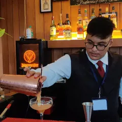 A bartender in classic uniform, focused on his craft as he pours a freshly shaken cocktail. We pride ourselves on the precision and care we put into every single drink.