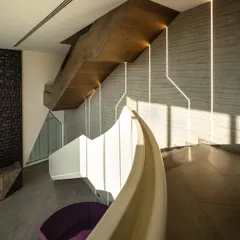 This sculptural staircase serves as a central feature, connecting the different levels of the office. The interplay of the curved white balustrade with the angular wooden structure and integrated lighting creates a dynamic visual journey.