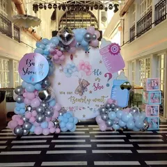 A large-scale "He or She, We can Bearly wait" baby shower theme in a spacious hall. The setup includes a round backdrop, pink and blue balloon arrangements, and themed props like "BABY" blocks.