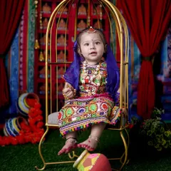 Here is a little Radha in a stunning, colorful lehenga, seated in a golden birdcage prop. The vibrant backdrop and traditional matki complete the look for this festive portrait.