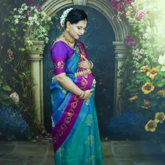 A regal studio portrait of a mom-to-be in a beautiful blue and purple silk saree. The floral backdrop adds a touch of softness to this traditional look.