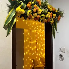 A festive housewarming entrance, with a doorway adorned with marigold garlands and a curtain of fairy lights creating a warm welcome.
