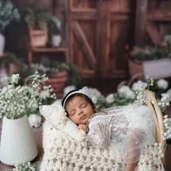 This wider shot shows the complete setup, with the baby nestled in a cozy knit basket surrounded by white flowers. The rustic wooden background adds warmth to this angelic scene.