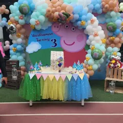 The main cake table setup for a Peppa Pig party, celebrating Vardhaman turning three. The backdrop and colorful table skirt create a cheerful and inviting scene.