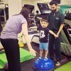 A therapist provides gentle support to a young child balancing on a BOSU ball. This exercise is excellent for developing core stability and proprioception in our pediatric clients.