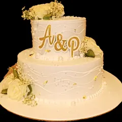 A timeless two-tier wedding cake that exudes elegance. Featuring classic white frosting with subtle texturing, delicate white roses, baby's breath, and personalized gold monogramming, this cake is perfect for celebrating your special day.