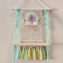 A cheerful wall shelf designed for a child's room. It features a pastel rainbow and colorful tassels, making it a fun place to store small toys or books.