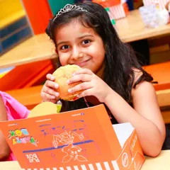 A happy girl enjoying a burger from her own Play Box meal box. We make mealtime fun too!