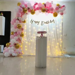 A lovely backdrop for a home party, using a curtain of fairy lights and a pink and gold balloon arch.