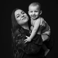 A classic black and white portrait of a mother and her smiling baby. The dark background makes their expressions of pure joy really stand out.