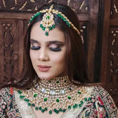 A detailed shot of a heavy Kundan choker and matha patti set with green stones and beads. This shows the kind of statement pieces available for your bridal shoots.