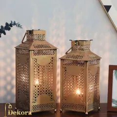 A pair of golden metal lanterns with intricate latticework. Inspired by Moroccan design, these holders cast beautiful shadows and add a warm, exotic touch to any space.