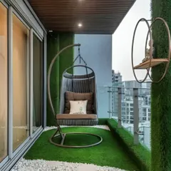 This cozy balcony features a comfortable swing chair, perfect for relaxing with a view. The artificial grass floor and green wall panels create a garden-like feel in a compact urban space.