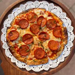 A top-down view of our signature pepperoni pizza, served on a wooden board with a delicate paper doily. The cheese is perfectly melted over the crisp pepperoni slices, ready to be enjoyed.