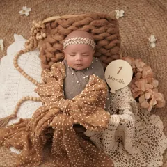 An adorable one-month-old baby girl sleeps peacefully in a basket, styled with a large polka-dot bow and a sign marking her milestone.