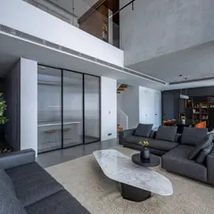 The living area of 'The Grey House', a duplex apartment in Mumbai. We embraced a minimalist aesthetic with a monochromatic grey palette, using textured walls and clean-lined furniture to create a space that is both sophisticated and calming. The double-height ceiling enhances the sense of openness and light.