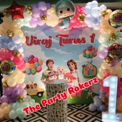 This Cocomelon theme for a first birthday features a pastel balloon arch and a backdrop with all the favorite characters. The light-up number '1' and themed cake stand complete the look.