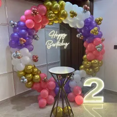 A vibrant and colorful ring decoration for a second birthday party, featuring pink, purple, and gold balloons with a light-up '2' marquee number.