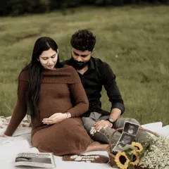 A beautiful, full-scene shot of the couple enjoying their maternity picnic in a field. They are looking down at the baby bump together, lost in their own world.