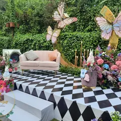 The main seating area, designed to feel like a scene from a storybook. It features a checkerboard stage, a pale pink sofa, and giant butterflies fluttering against a backdrop of lush greenery.