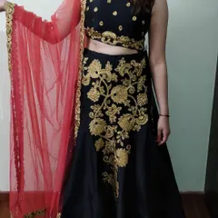 Our classic black lehenga paired with a bright red net dupatta offers a timeless look. The skirt features prominent gold floral embroidery, making it a versatile outfit for any evening wedding function or festive party.