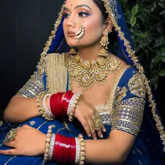A seated portrait of a Rajputi bride in a royal blue lehenga. The makeup features a pop of blue eyeliner to match the outfit, creating a cohesive and stunning look.