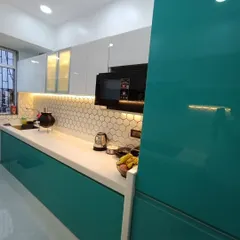 This kitchen features a striking combination of teal green acrylic on the lower cabinets and white on the upper ones, complemented by a modern hexagonal tile backsplash and warm under-cabinet lighting.