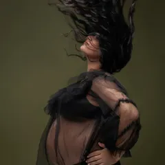 A dynamic and freeing moment captured in the studio. The sheer black top and dramatic hair flip add a sense of movement and confidence to this powerful maternity shot.