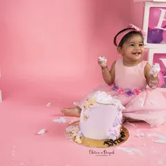 A happy baby girl enjoying her first taste of cake during her pink and purple themed cakesmash photoshoot in our Bangalore studio.