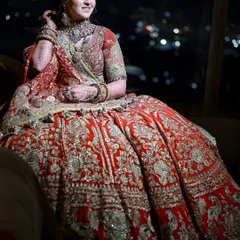A quiet moment before the ceremony. The rich embroidery of the red lehenga is perfectly complemented by the way the dupatta is draped over the shoulder, framing her beautifully.