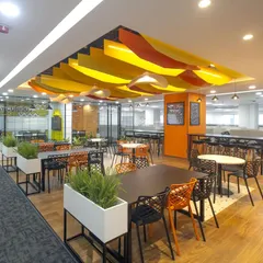 The canteen at Scientific Games, viewed from the main workspace. The area is defined by wood-look flooring and planters, creating a distinct zone that feels like a cafe within the office.