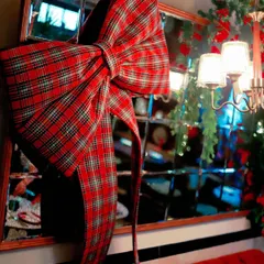 A giant, oversized plaid bow serves as a statement piece on a mirrored wall, adding a touch of rustic charm to the elegant Christmas setup.