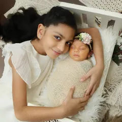 An older sister lovingly holds her newborn sibling, who is nestled in a miniature crib. This shot combines a sibling portrait with one of my themed setups.