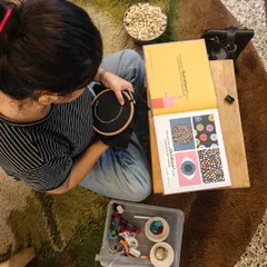 A parent works on an embroidery piece, drawing inspiration from a book. Each stitch in our community canopy represents a story and a hope for the children stepping out into the world from our school.